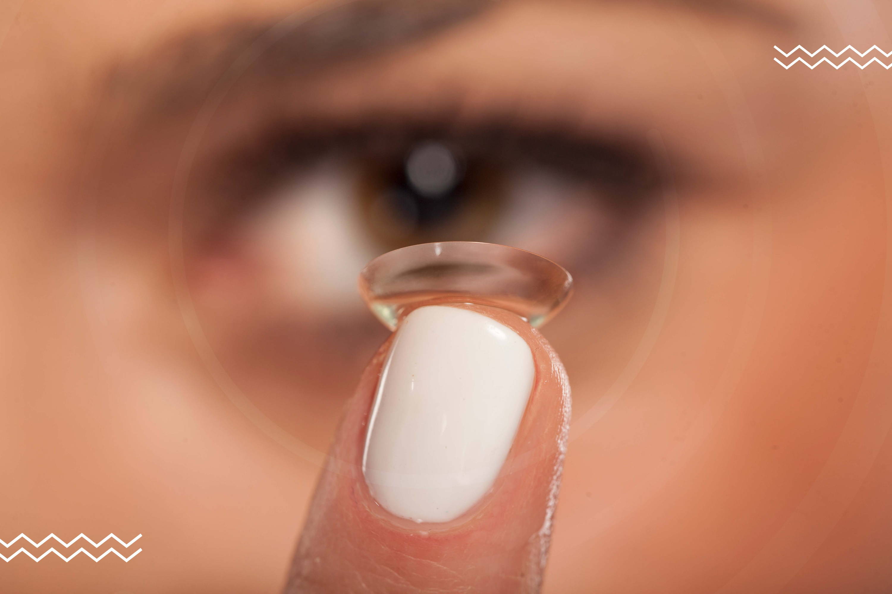 Una mujer mira directamente a la cámara mientras sostiene un lente de contacto con su dedo índice.