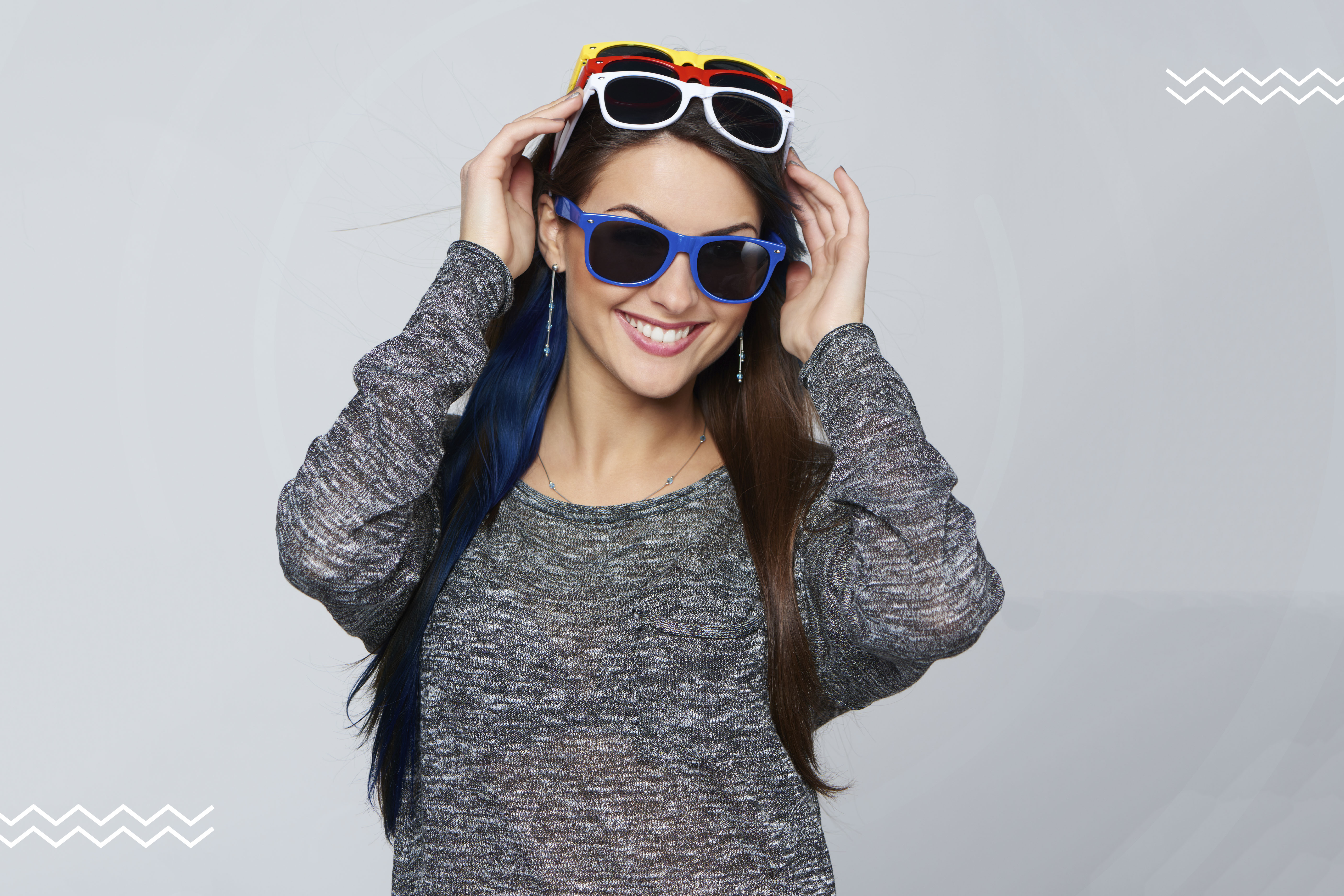 Imagen de una mujer joven que se está probando feliz diferentes opciones de lentes de sol.